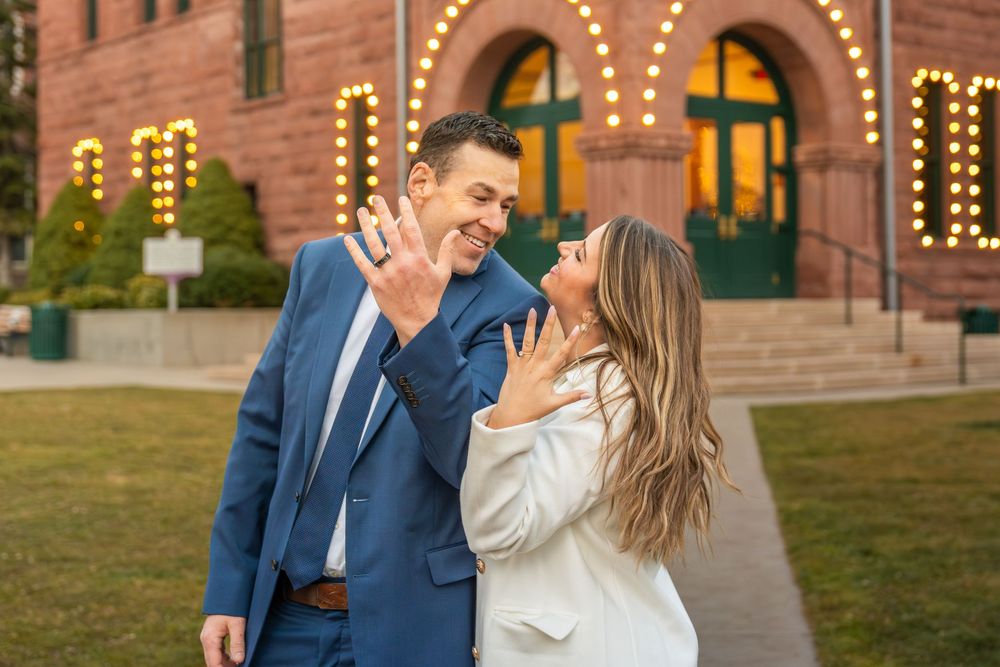 A joyful couple celebrating their engagement in front of a historic brick building.