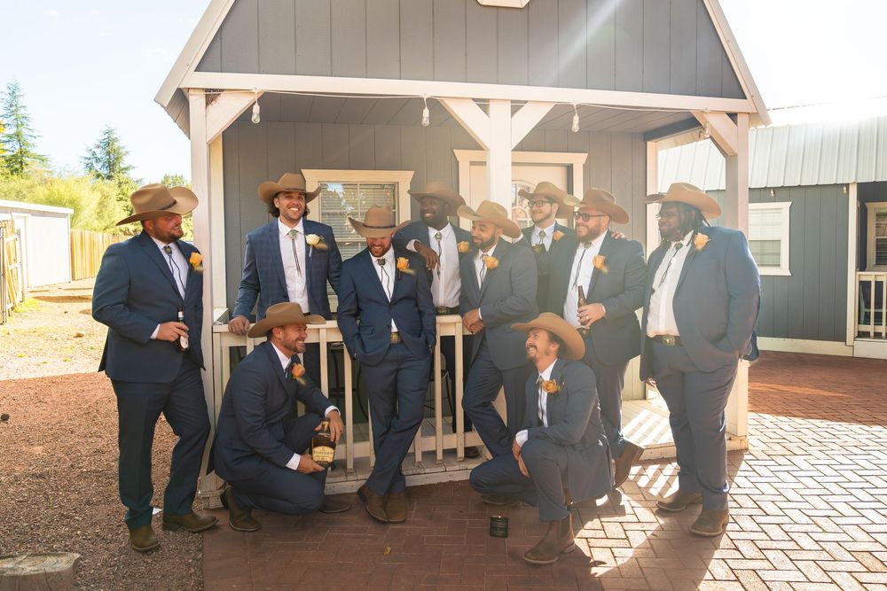 A group in formal attire poses together under a wooden gazebo in warm sunlight.