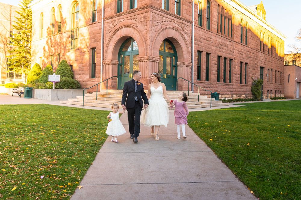 Wedding party walks along historic red brick building exterior during golden hour.