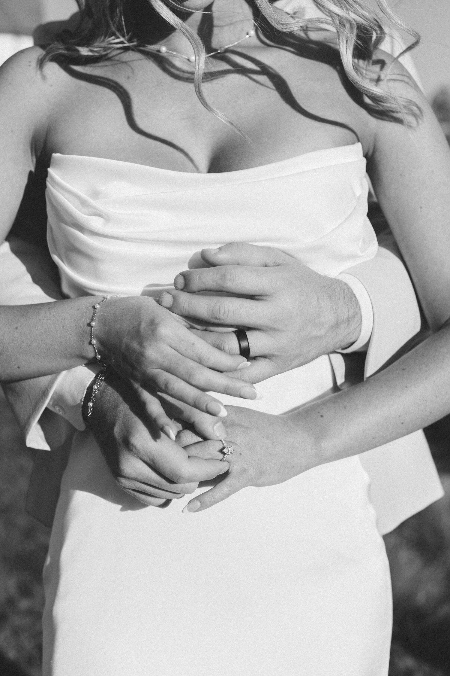 Close-up view of hands wearing wedding rings against a white dress background in elegant bridal photography.