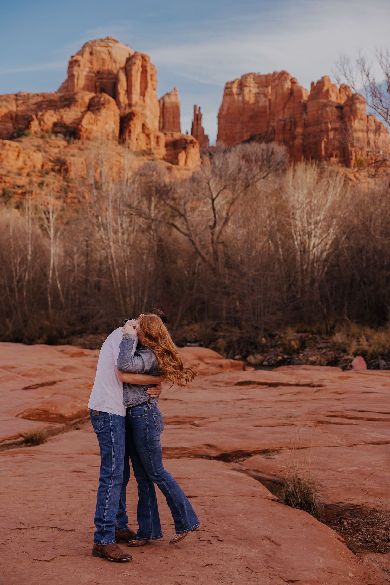Couple sharing an intimate moment on red rocks with dramatic desert cliffs in the background.
