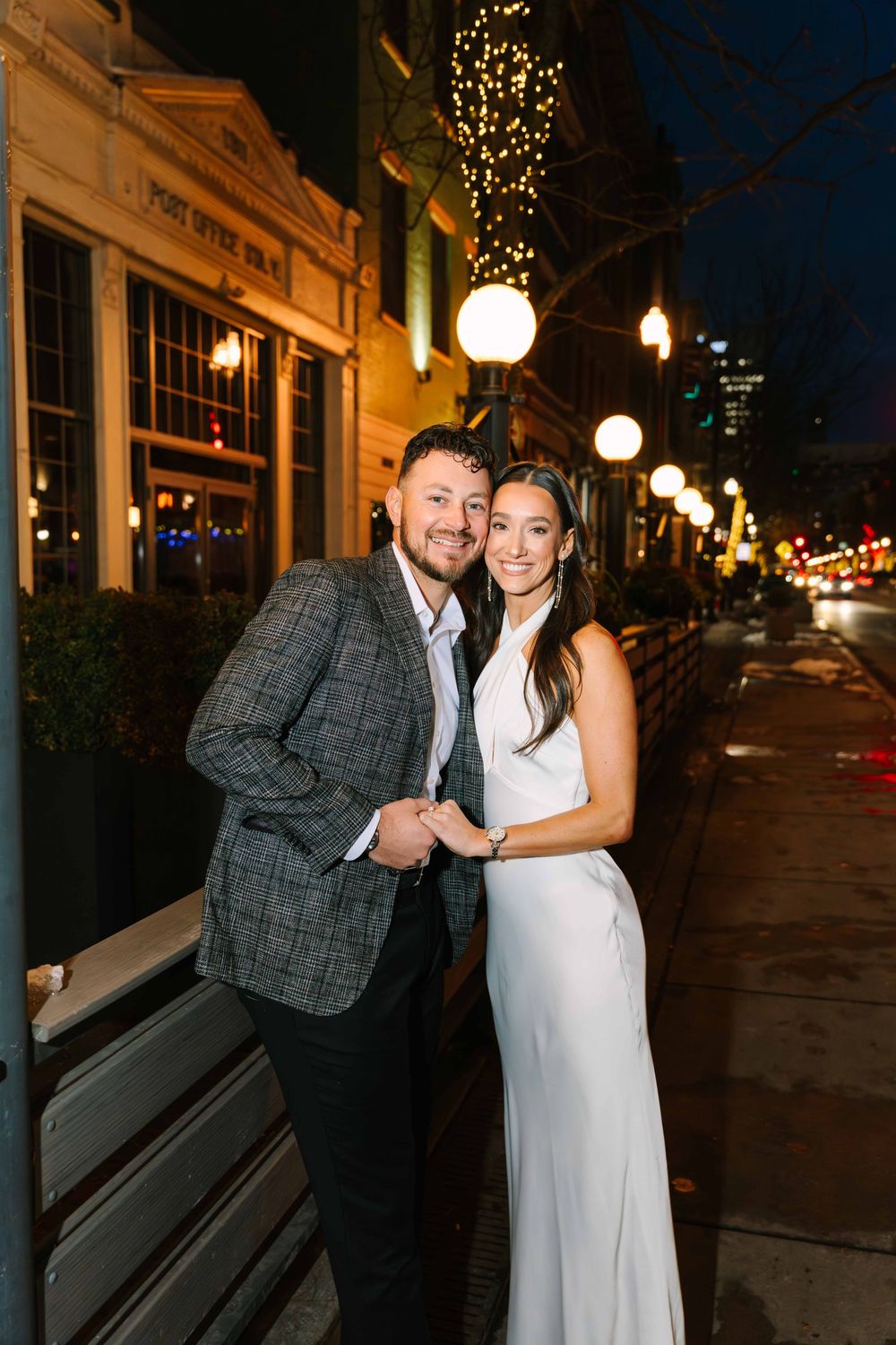 A romantic nighttime street scene with string lights illuminating a couple in formal attire.