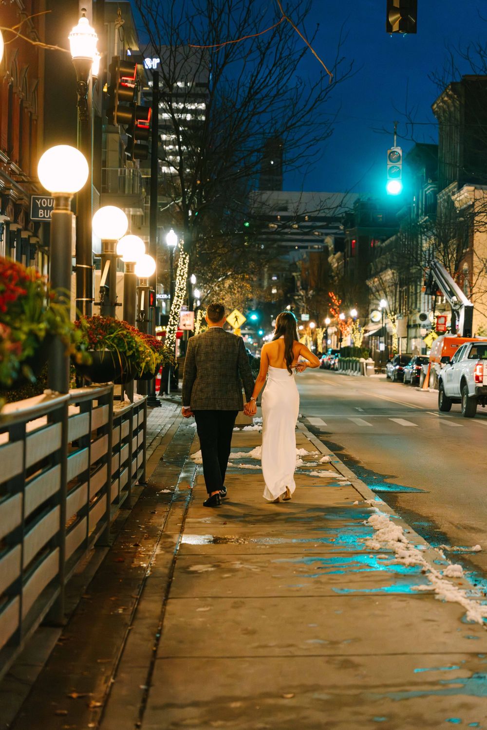 Illuminated city street at night with glowing lampposts and snow-covered sidewalks.