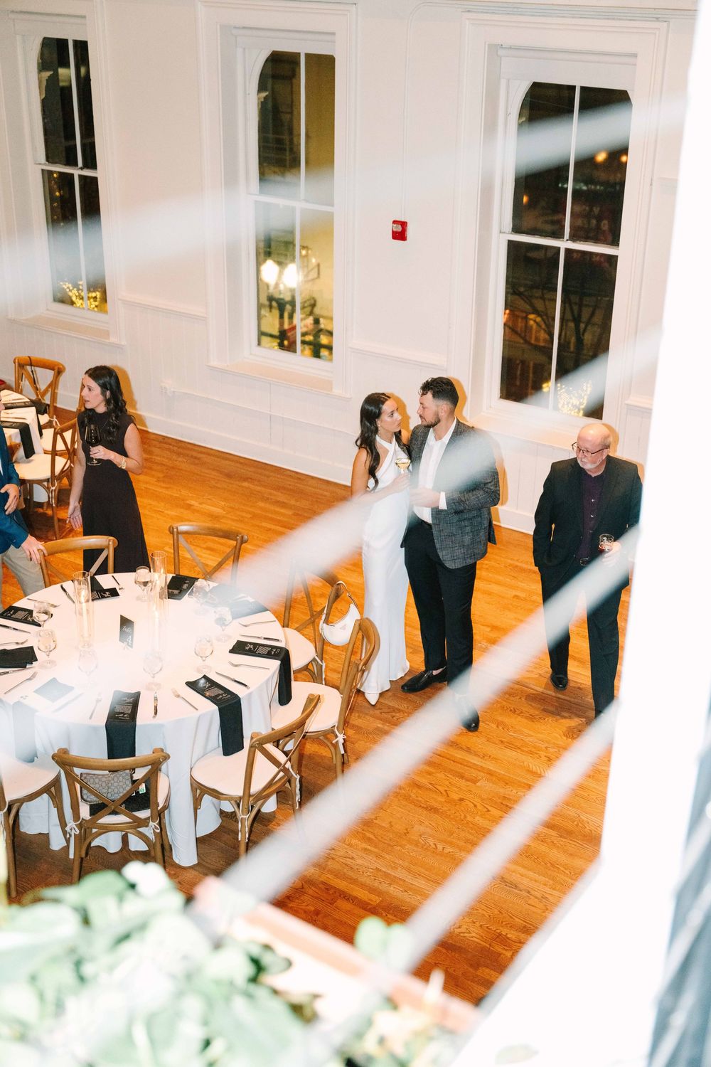 Wedding reception venue with hardwood floors and white walls showing guests mingling.