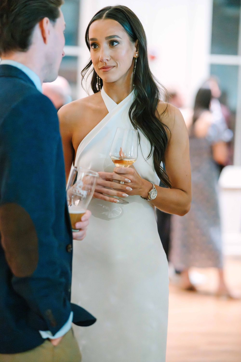 Woman in white dress holding a cocktail during an elegant reception.