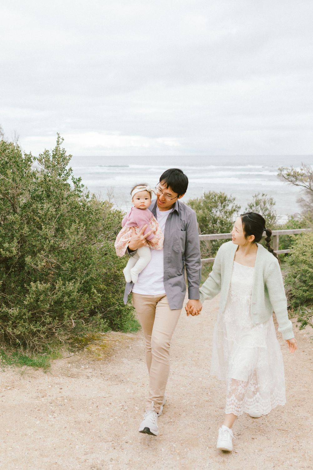 A family walks together along a scenic coastal path on a cloudy day.