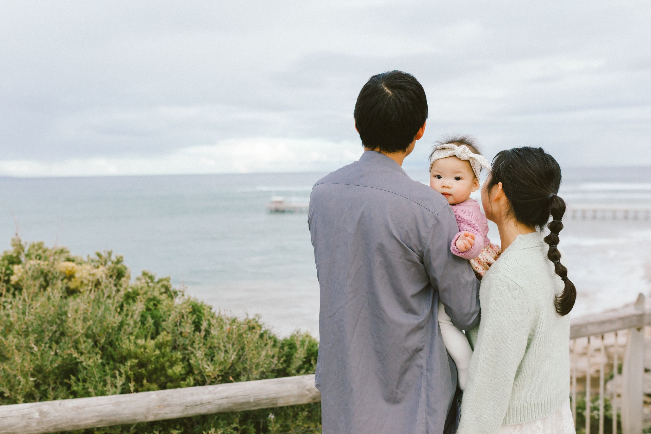 A couple in formal attire embraces while standing on a scenic coastal overlook during an intimate wedding ceremony.