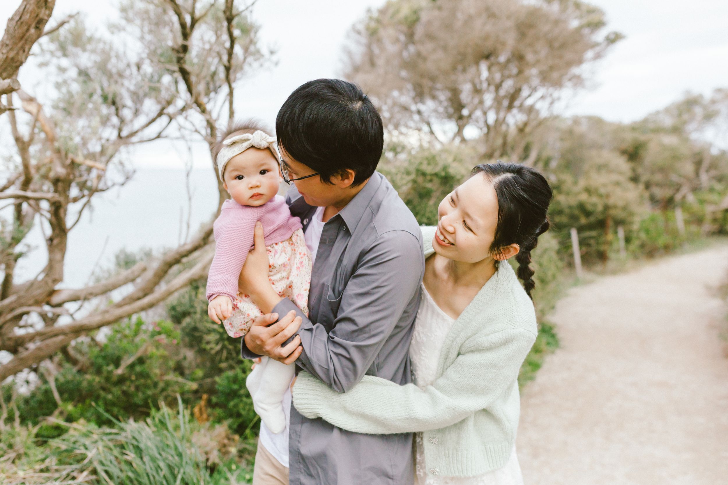 Family shares tender moments together while walking along a scenic coastal path on a bright sunny day.