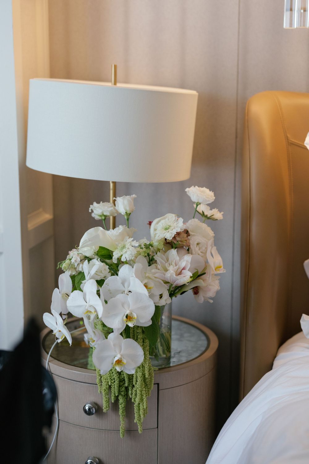 White orchids and floral arrangements displayed on side tables with white lampshades in an elegant interior setting.