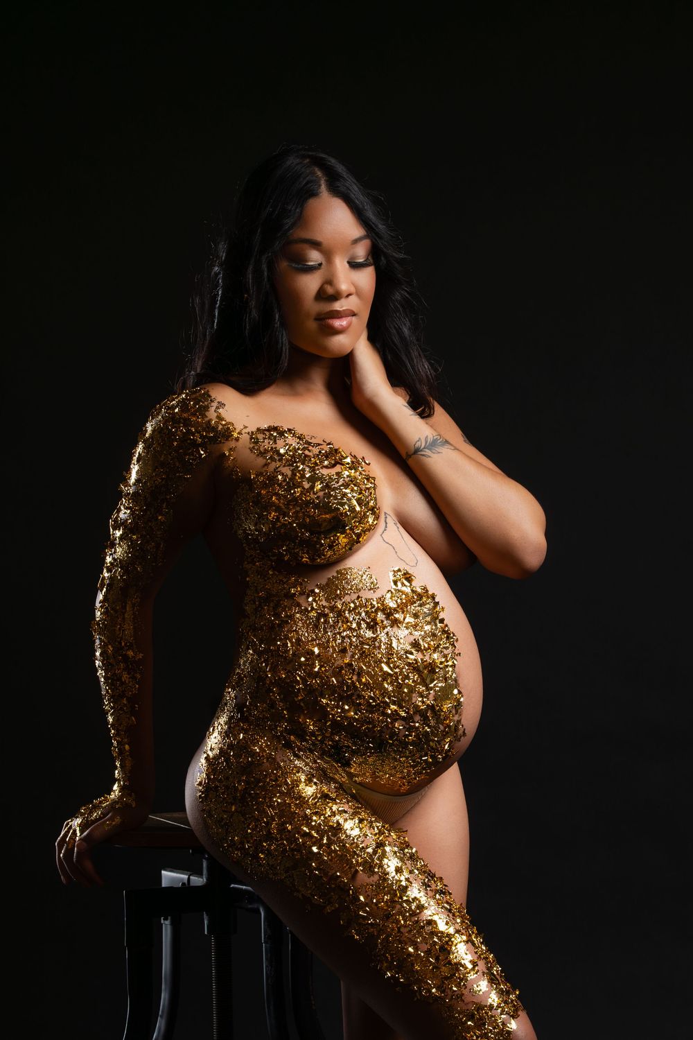 A maternity portrait featuring a glamorous gold sequined bodysuit against a dark background.