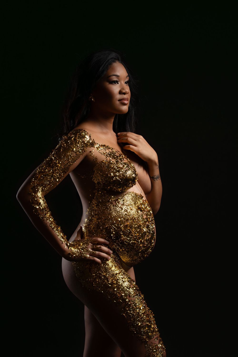 Artistic maternity portrait featuring a gold sequined bodysuit against a dark background.