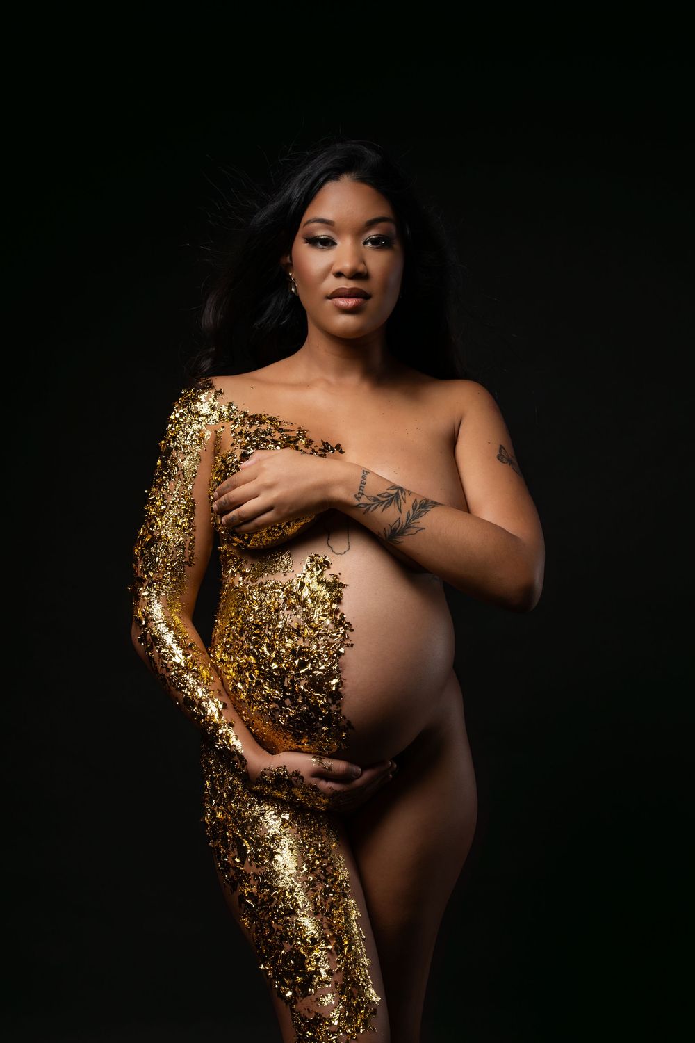 Artistic maternity photoshoot featuring gold glitter body paint against dark background.