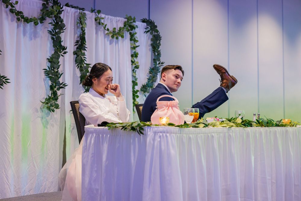 Bride and groom laughing at the wedding reception while the groom lifts his foot up