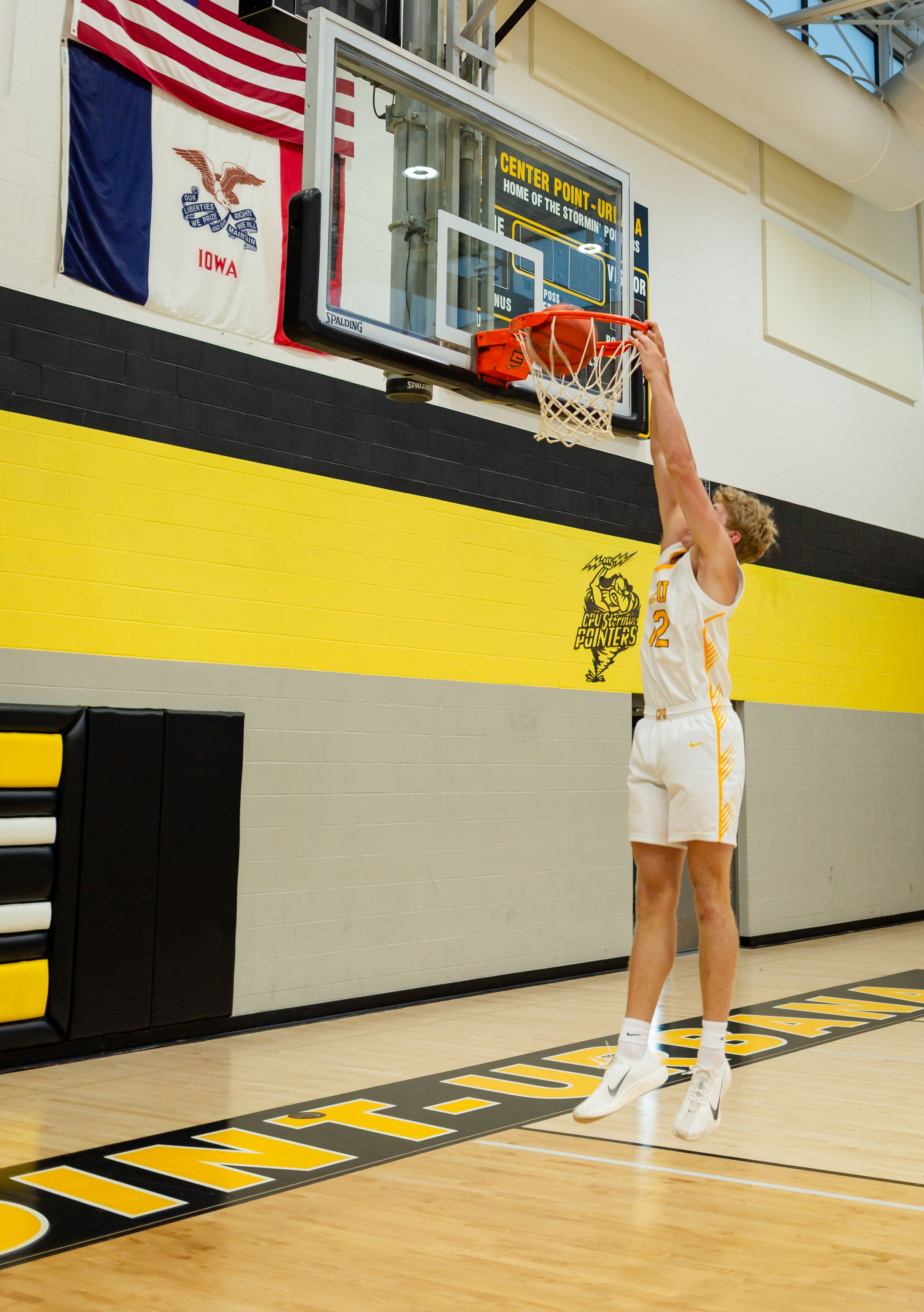 Basketball player in white uniform practicing free throws in a gymnasium with an American flag on the wall.
