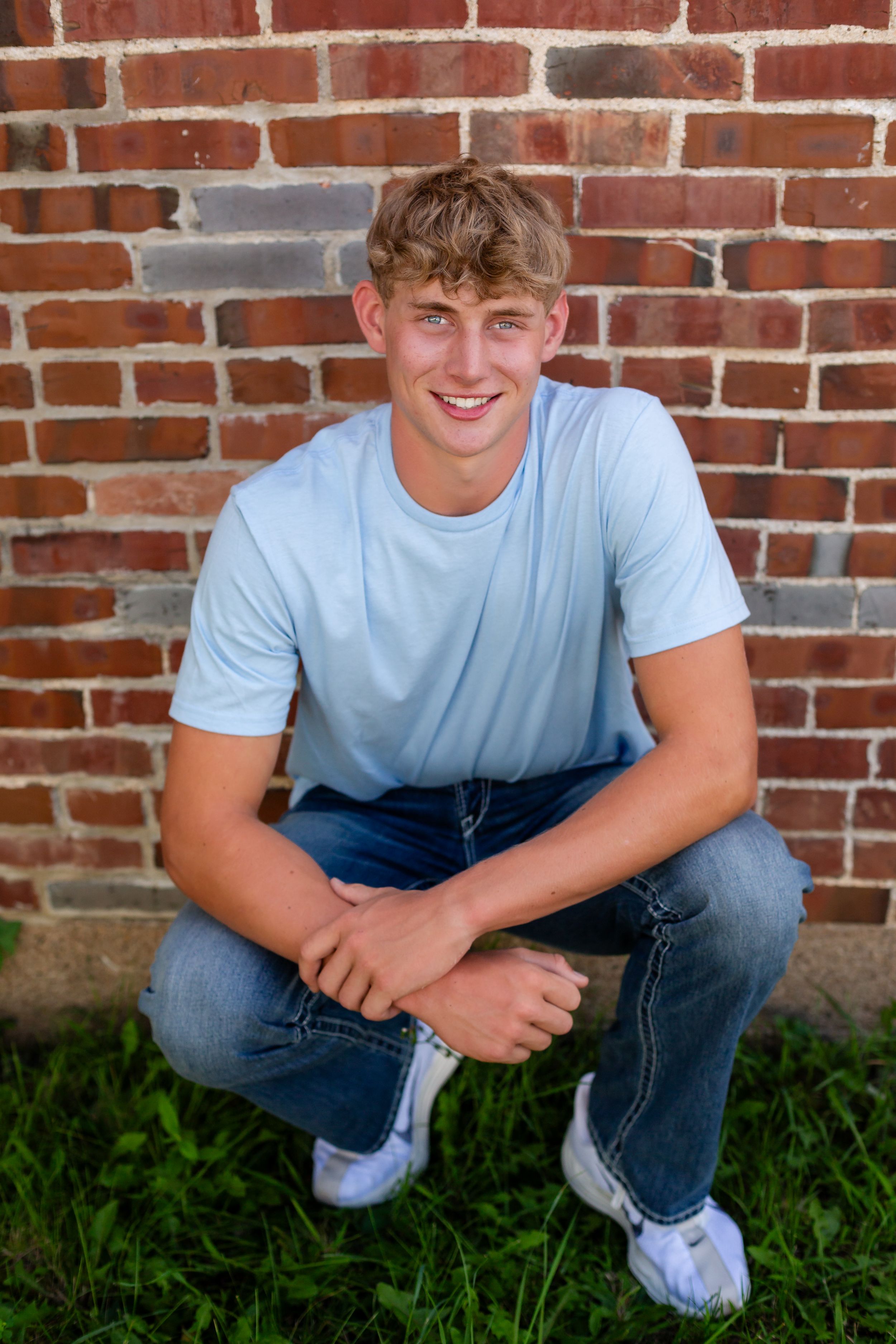 Four casual portraits of someone crouching against a brick wall wearing jeans and a light blue t-shirt.