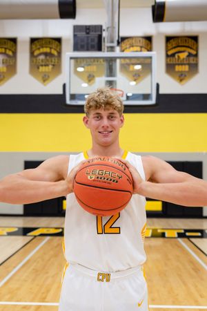 Basketball player in white jersey poses with ball in gymnasium with yellow banners on wall.
