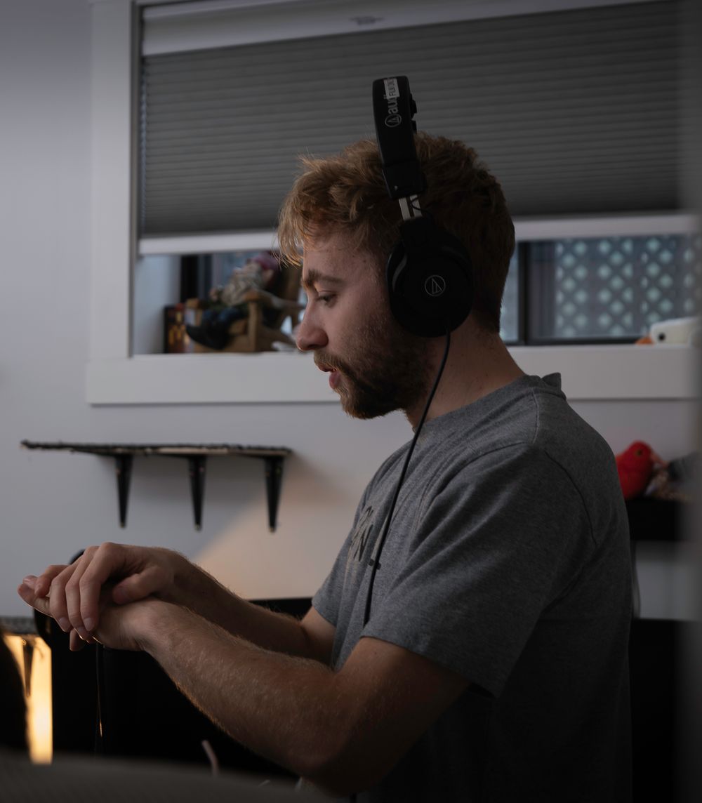 Person wearing headphones works at computer setup in dimly lit room.