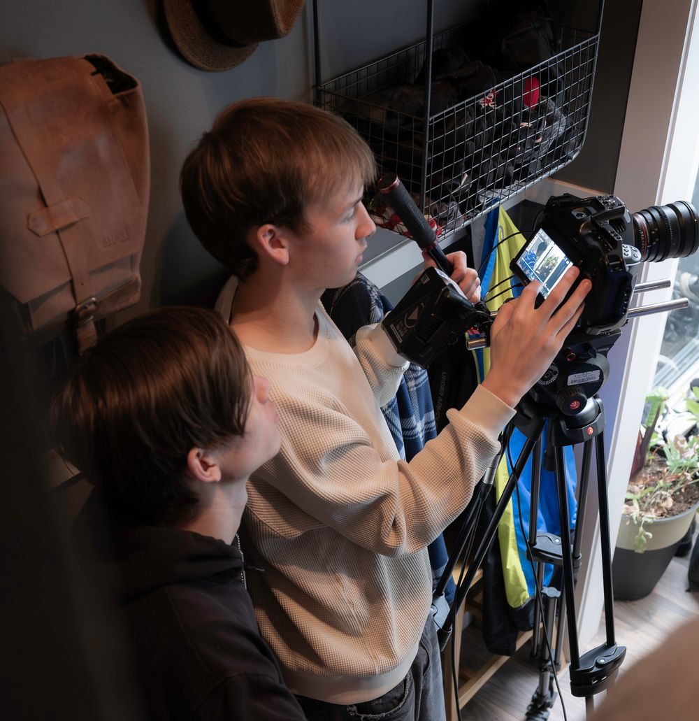 Camera operator filming against closet or storage area in indoor setting.