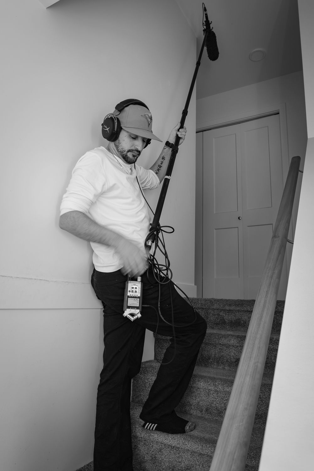 Sound technician in white shirt and headphones operates a boom microphone on stairs.