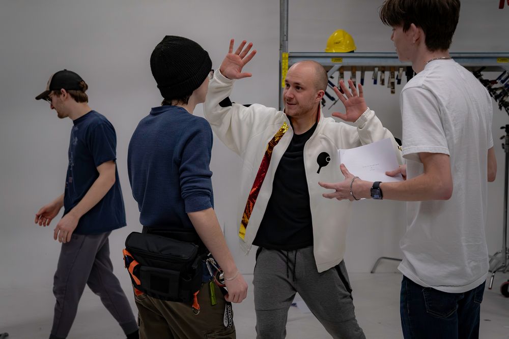 Creative team collaborating during a movement rehearsal in a white-walled studio space.