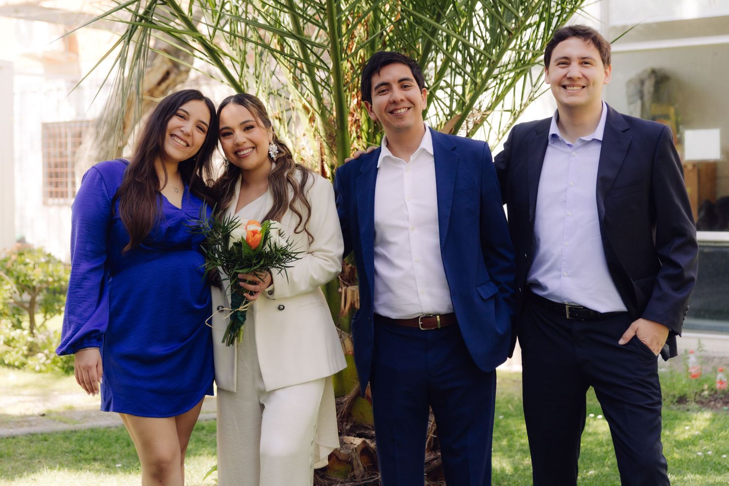 Smiling bride with bouquet poses with three guests in blue and casual attire outdoors.