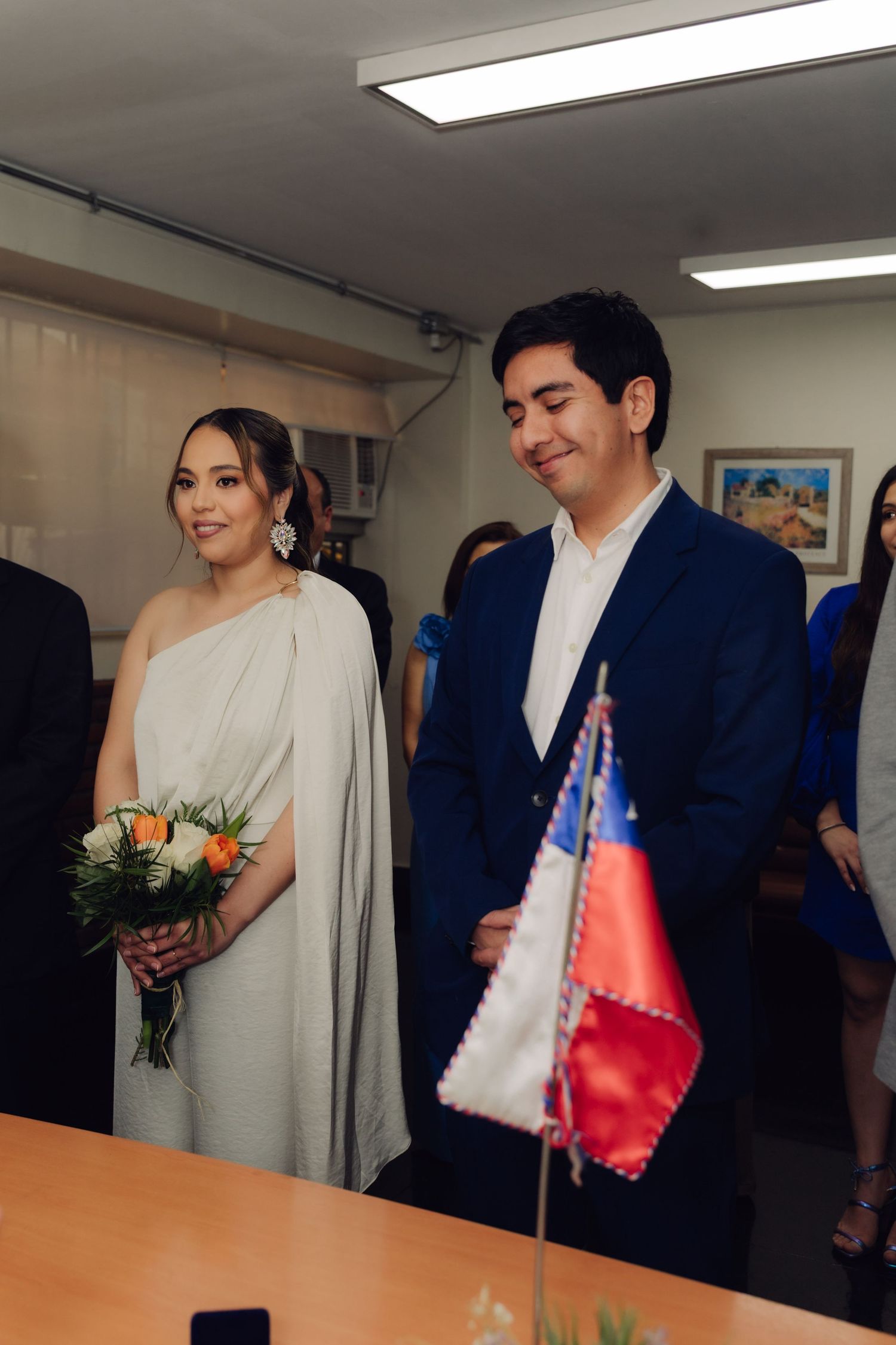 Bride in white gown holds bouquet beside groom in navy suit at civil ceremony.