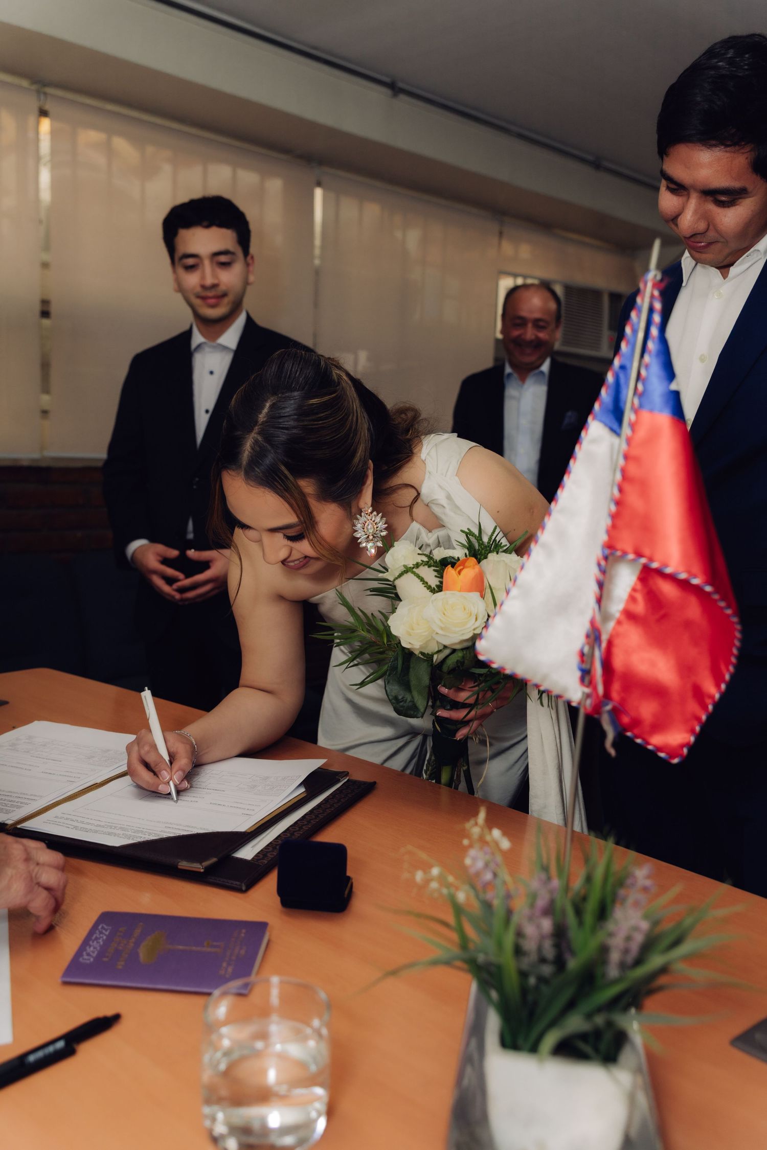 Bride signs marriage certificate while holding bouquet at official wedding ceremony.