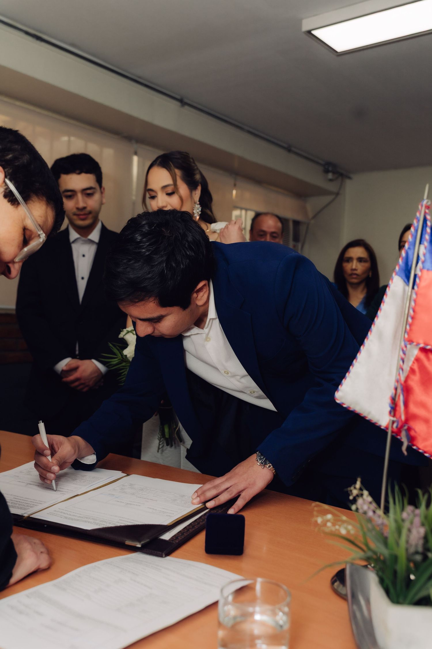Groom in navy suit signs marriage certificate at official civil wedding ceremony.