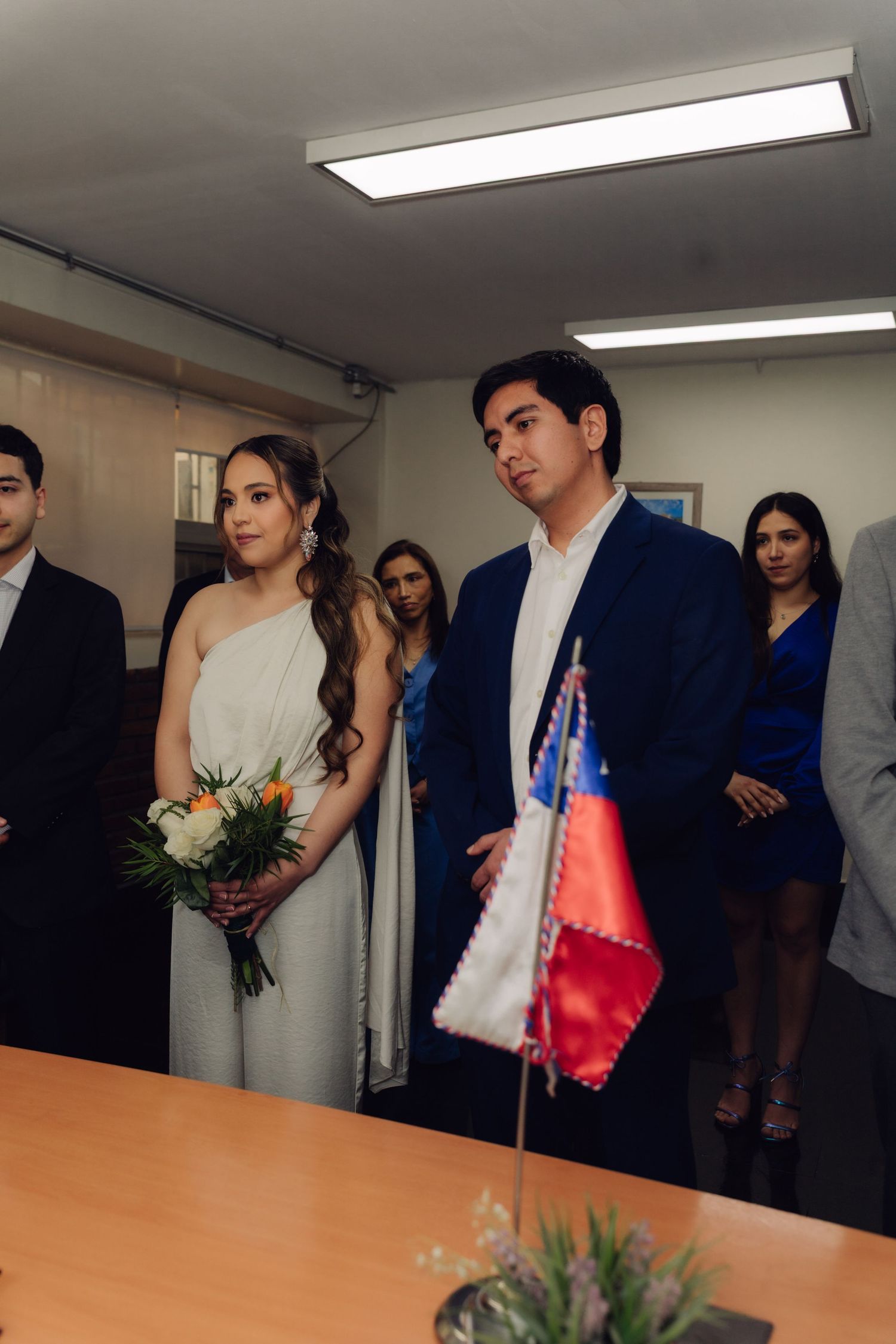 Bride in white gown and groom in navy suit stand at civil wedding ceremony.