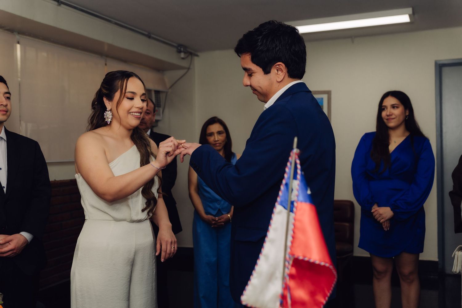 Groom sliding wedding ring onto bride's finger during civil marriage ceremony in Chile.