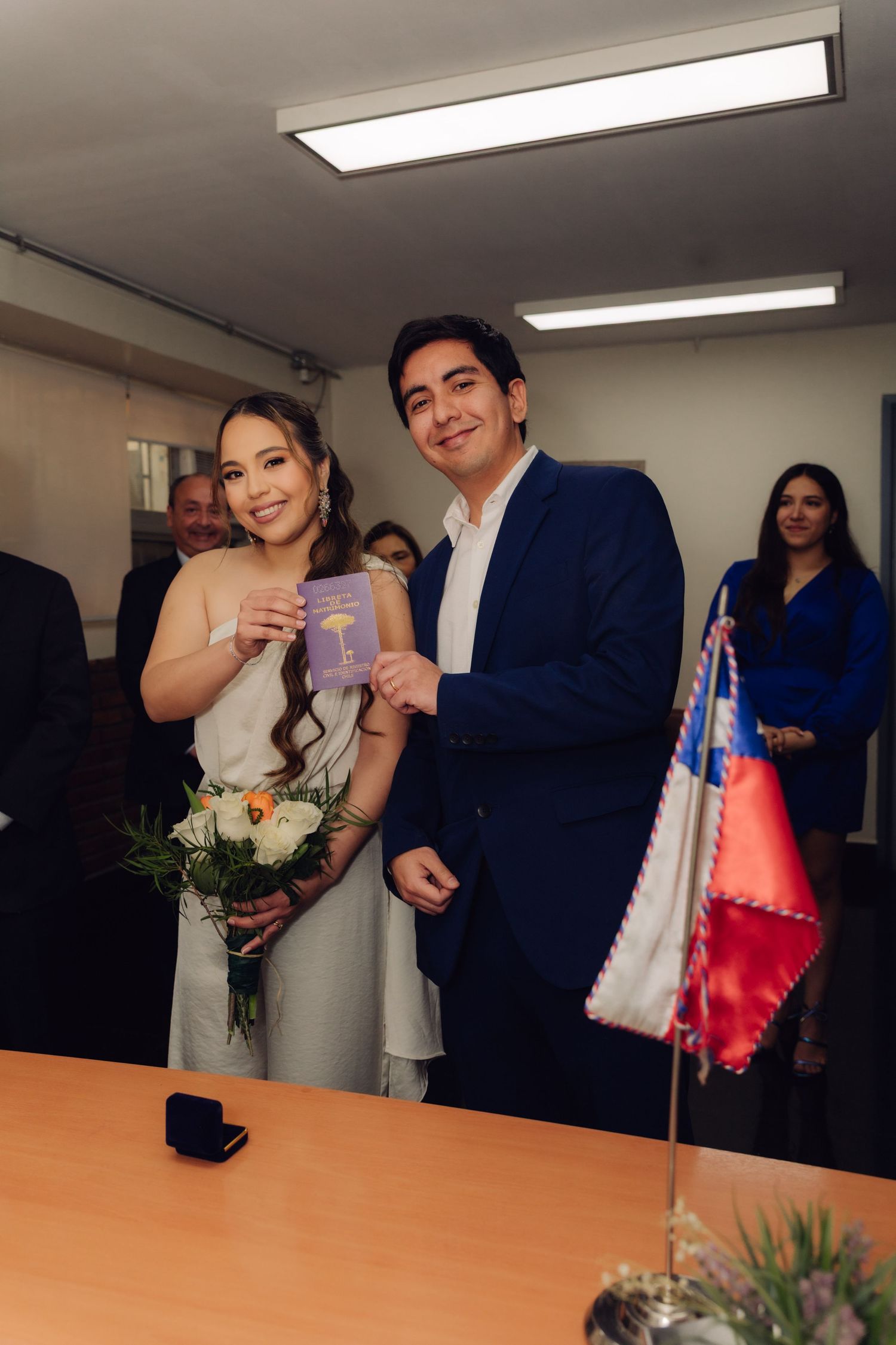 Newlyweds smiling and holding marriage certificate with Chilean flag at civil wedding ceremony.