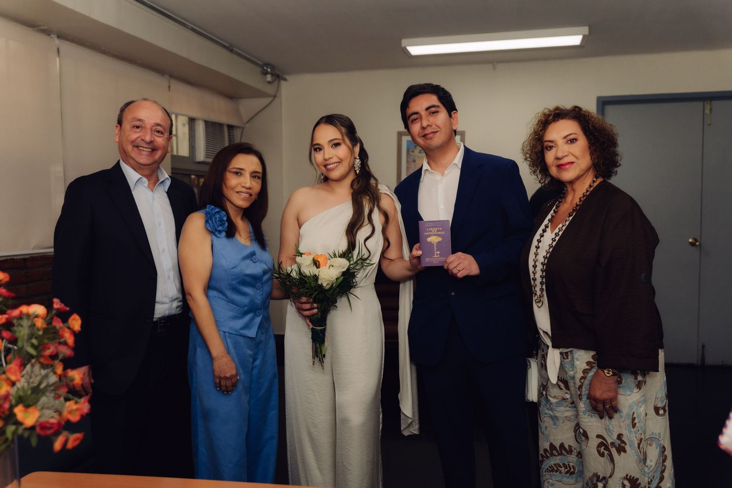 Wedding couple posing with family members holding bouquet and marriage certificate after ceremony.