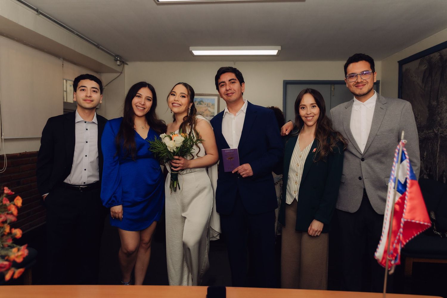 Newlyweds and wedding party posing for group photo with Chilean flag after civil ceremony.