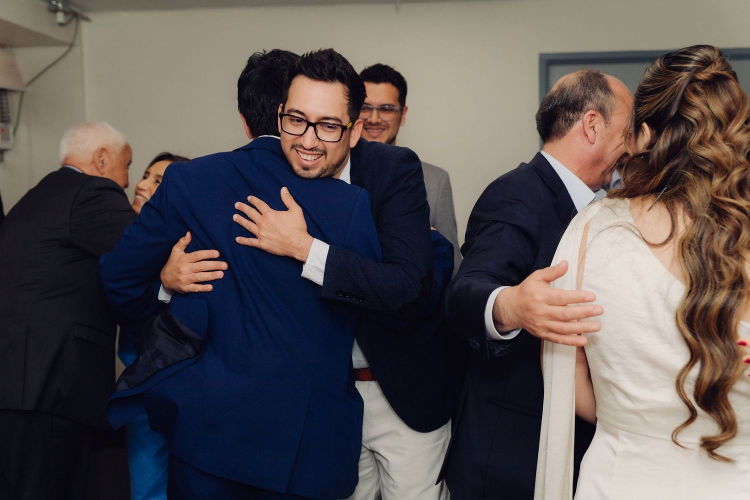 Joyful guests embrace and congratulate the newlyweds in a lively indoor wedding celebration.