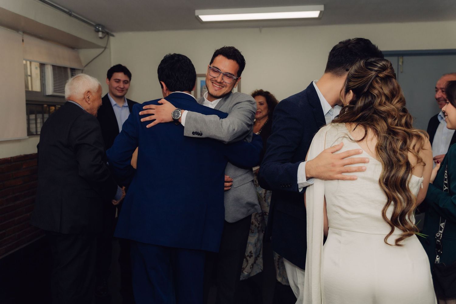 Wedding guests hugging and congratulating the newlyweds in a warm indoor celebration.