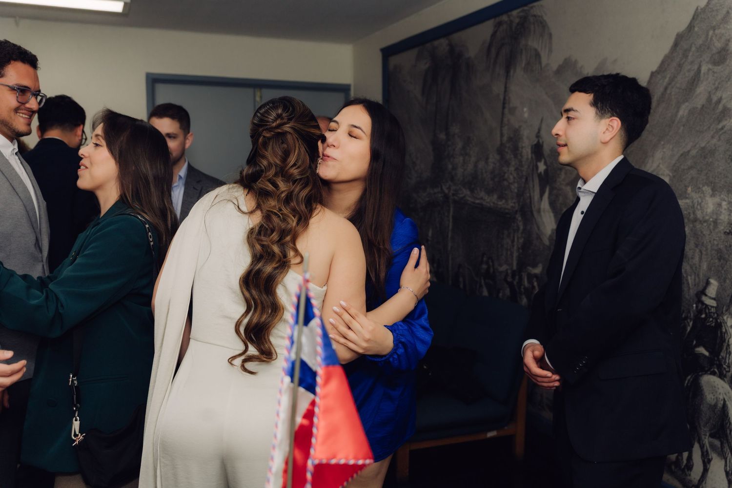 Bride in white gown exchanging a kiss on the cheek with a guest in blue dress at wedding.