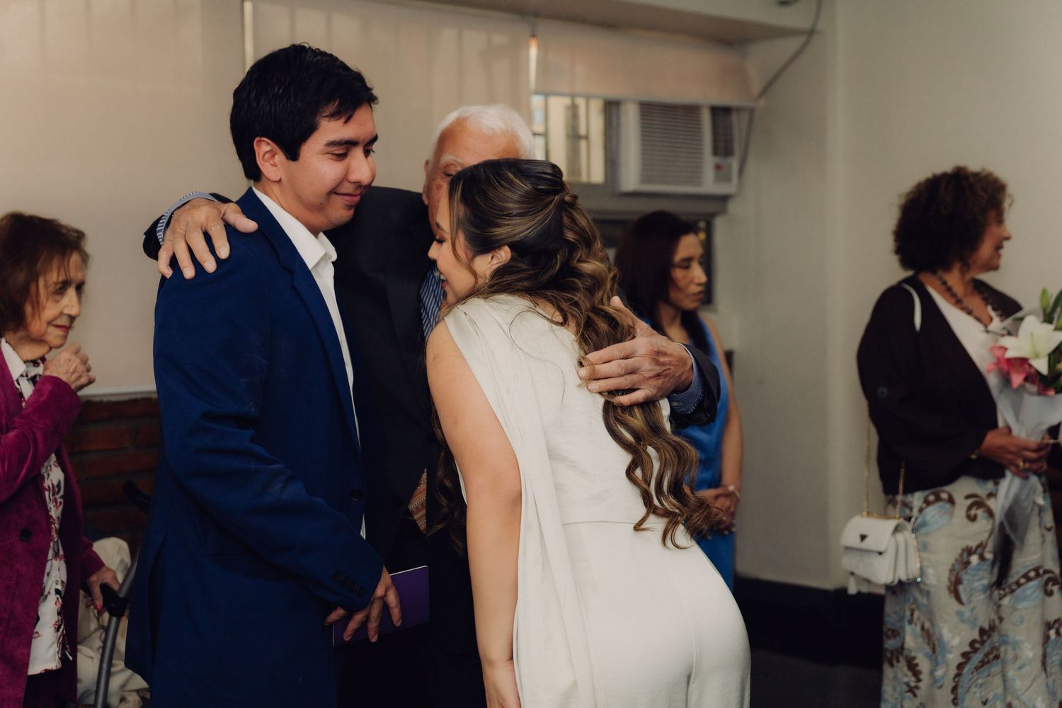 Bride and groom sharing an embrace with an elderly guest at their wedding reception.