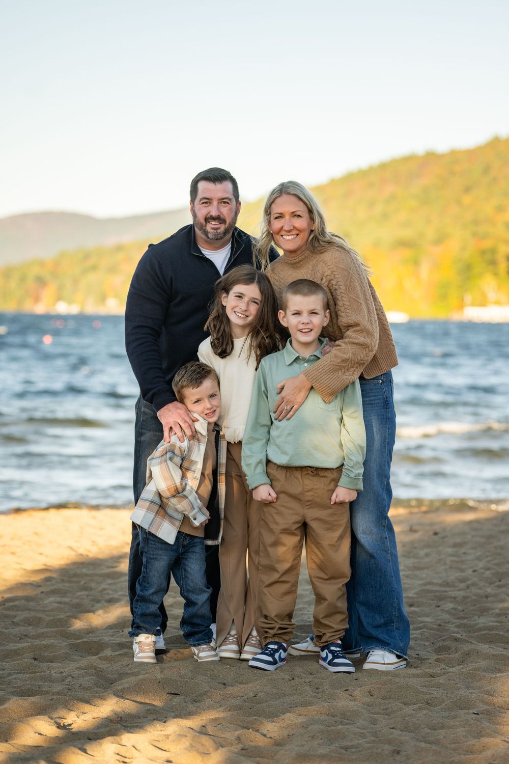A family poses together on a beach at sunset with mountains and water in the background.
