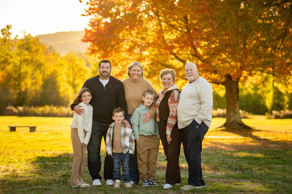 A group poses together outdoors during golden hour autumn sunset with fall foliage in the background.