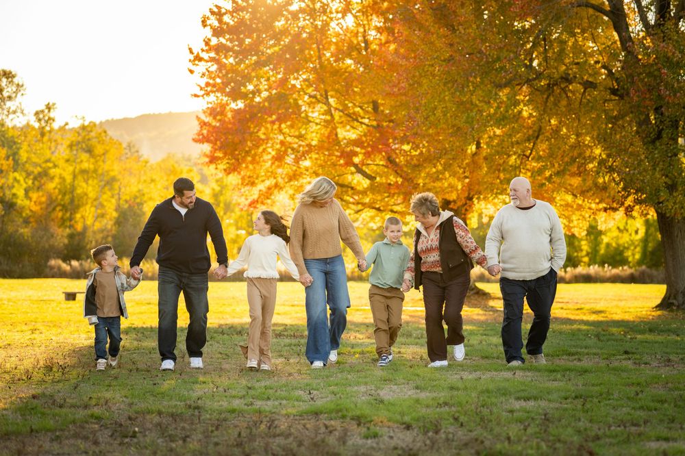 A group walks together holding hands across a sunlit autumn meadow with golden trees behind them.