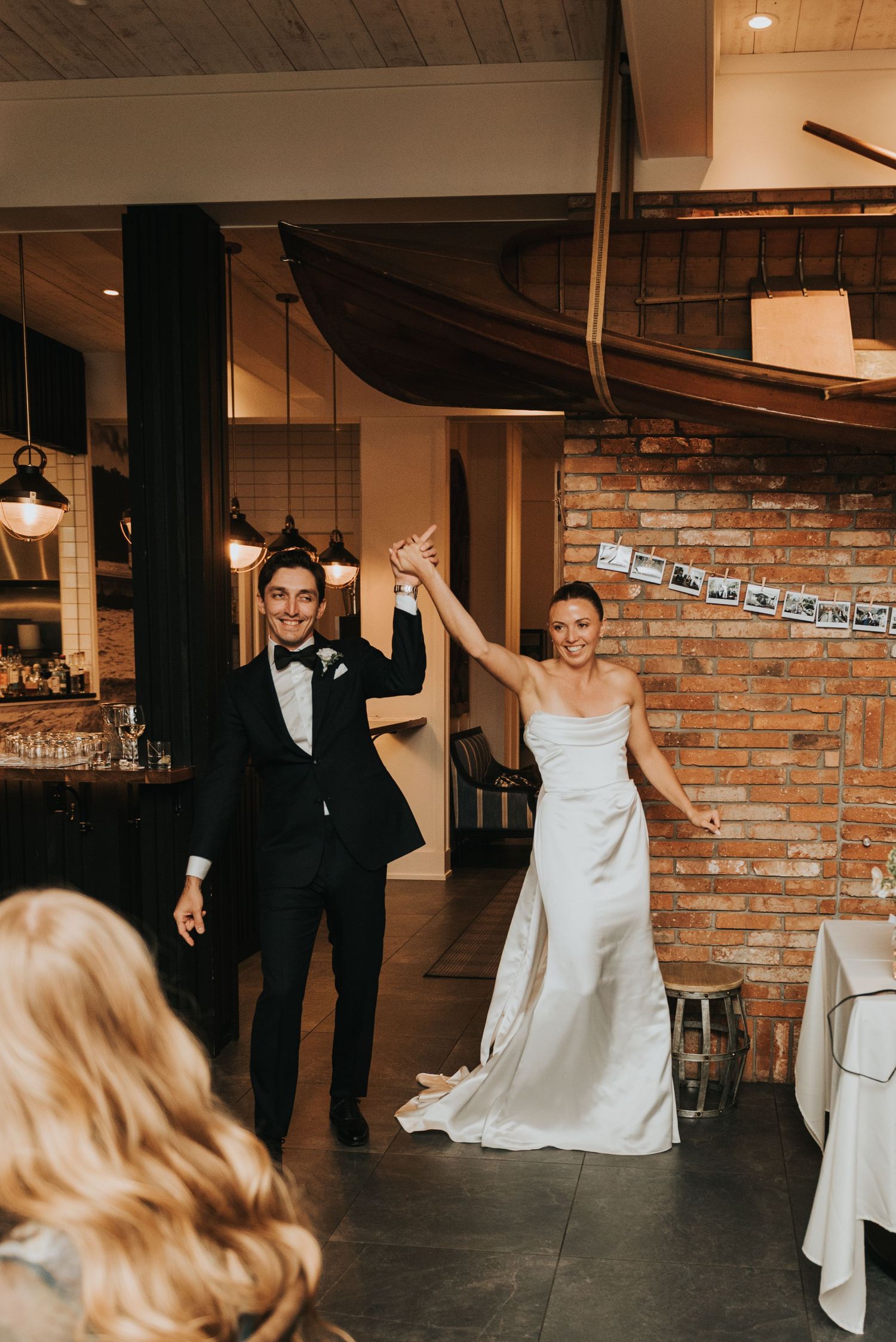 A couple celebrates their wedding entrance at a rustic venue with exposed brick walls and pendant lighting.