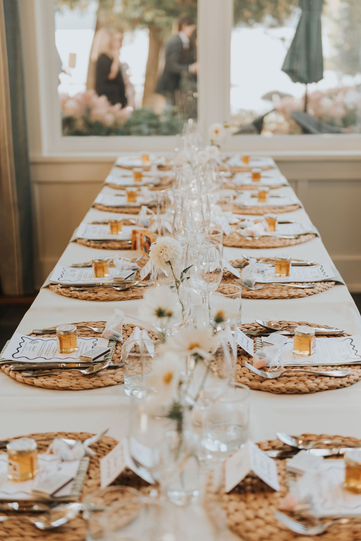 Elegant table setting with white linens, woven placemats, and delicate glassware arranged for a formal dining event.
