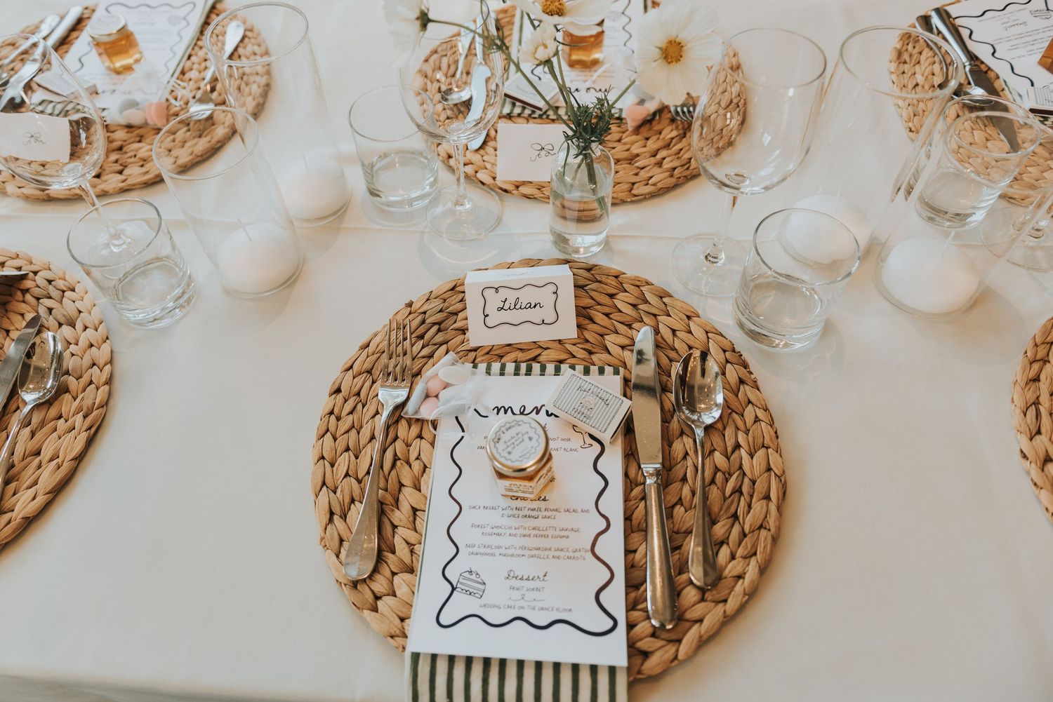 Elegant table setting with woven rattan charger plates, striped napkins and white tablecloth at a wedding reception.