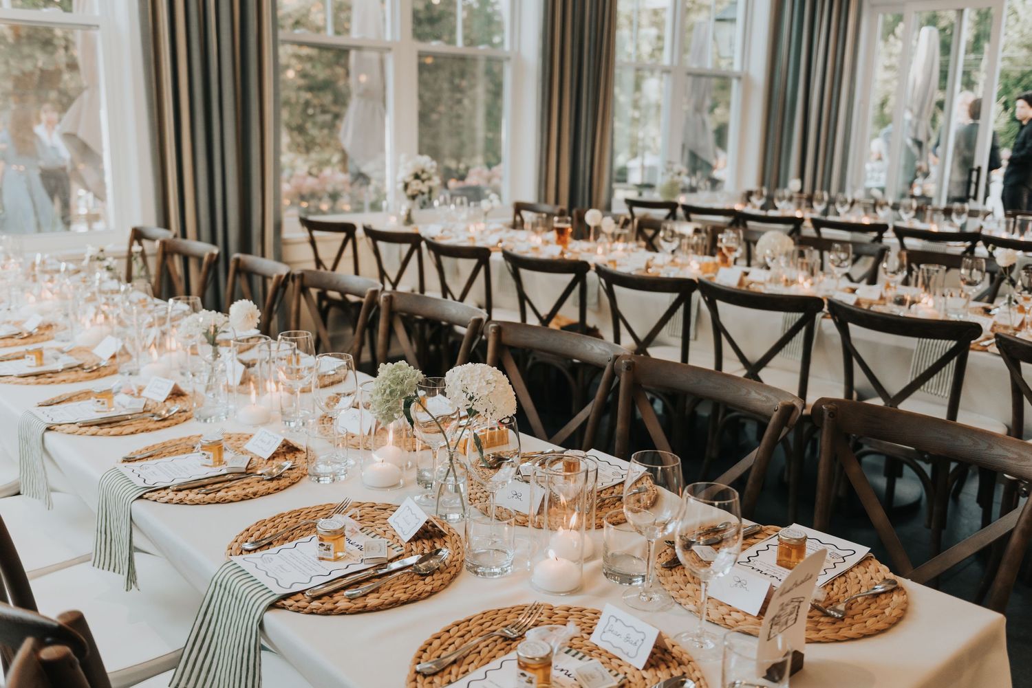 Elegant wedding reception tables set with gold chargers and floral centerpieces in a bright sunlit conservatory venue.