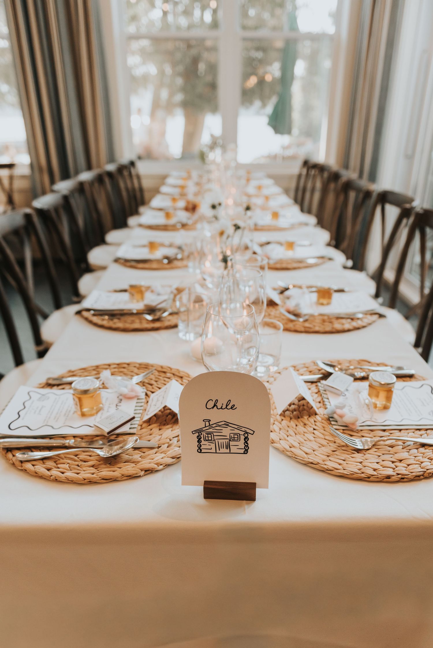 Long dining table decorated with natural woven chargers, white plates, and glass stemware for an upscale event.