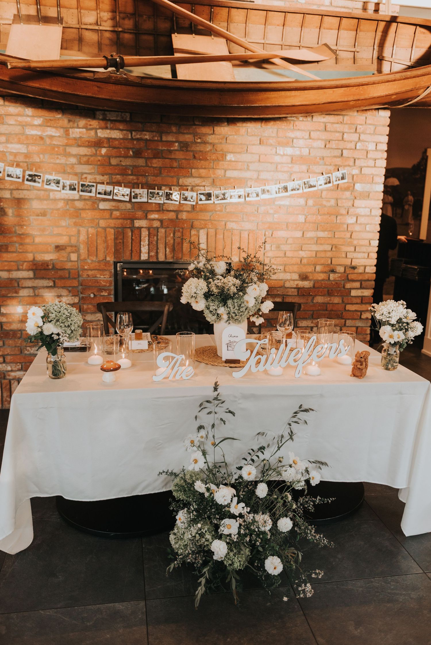 Elegant wedding reception tables with white linens and floral centerpieces against exposed brick walls in rustic venue.