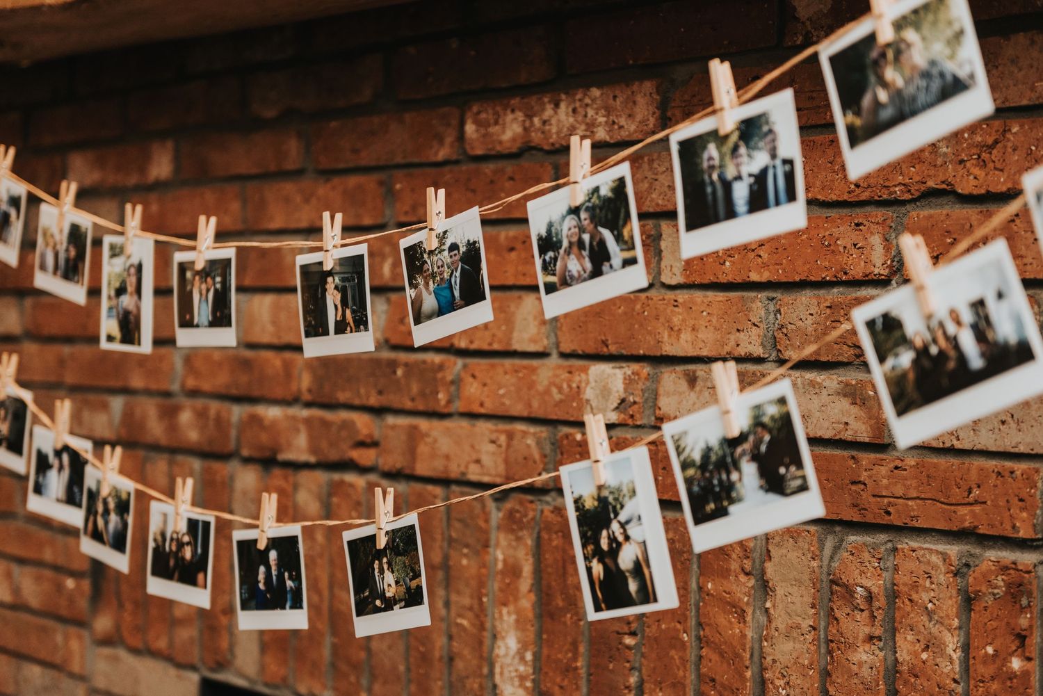 Black and white polaroid photos hanging on strings against a rustic brick wall create a nostalgic display.