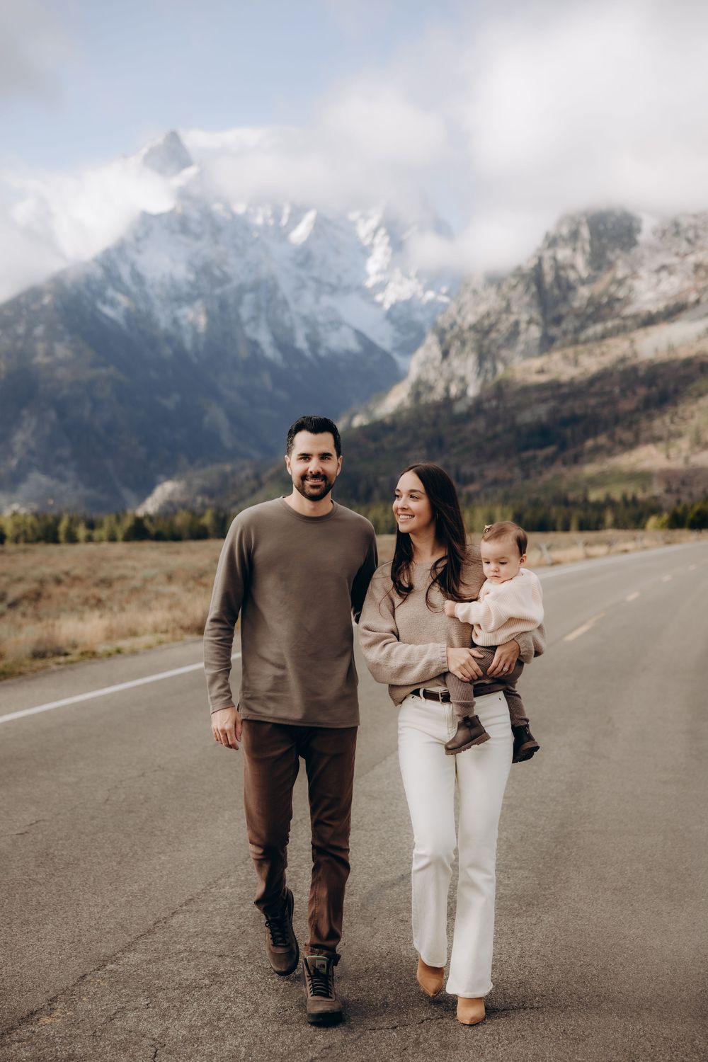 Family walking together on mountain road with snow-capped peaks in background during autumn season.