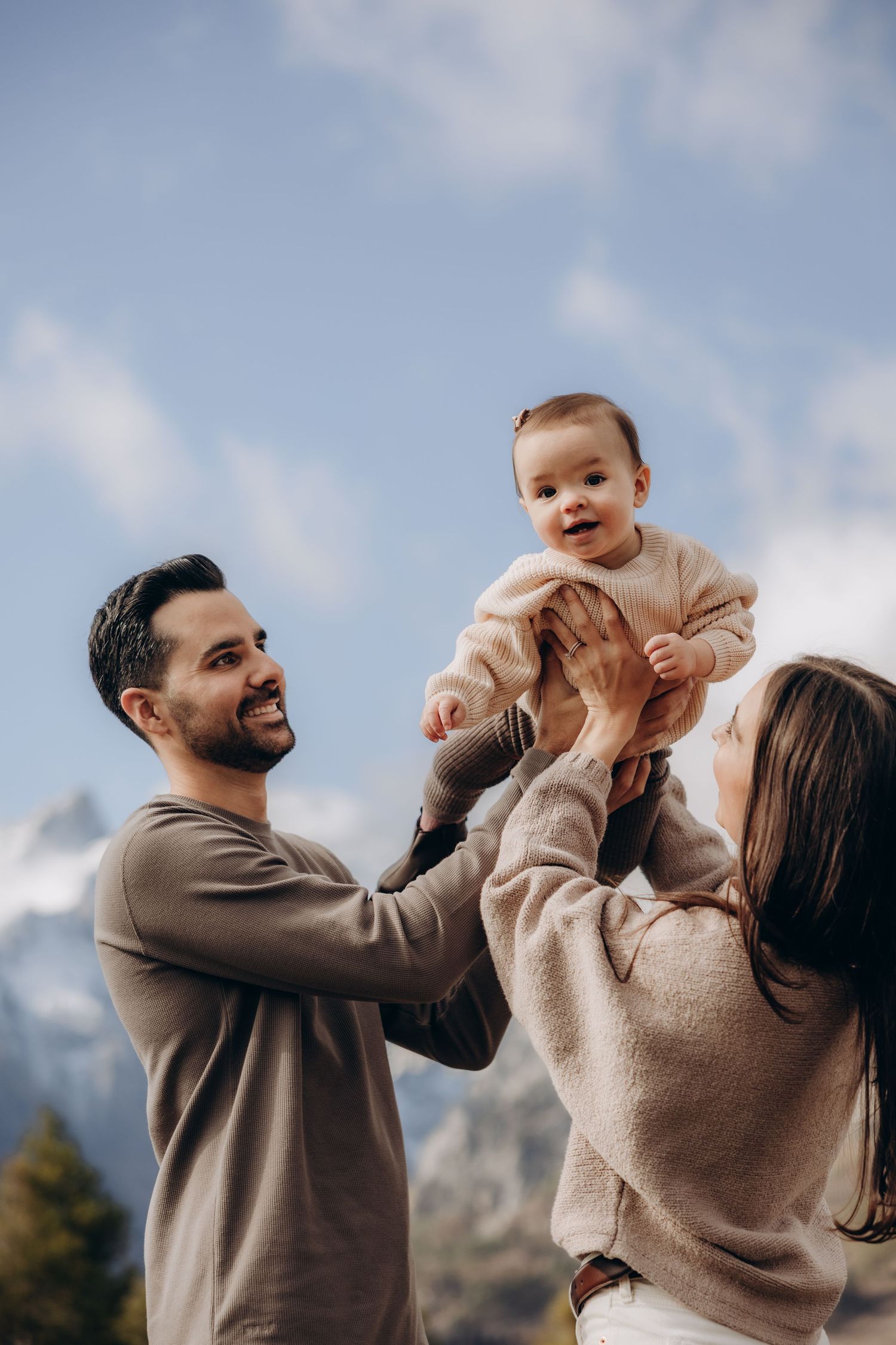 A happy family plays together outdoors against a mountain backdrop with cloudy blue skies.