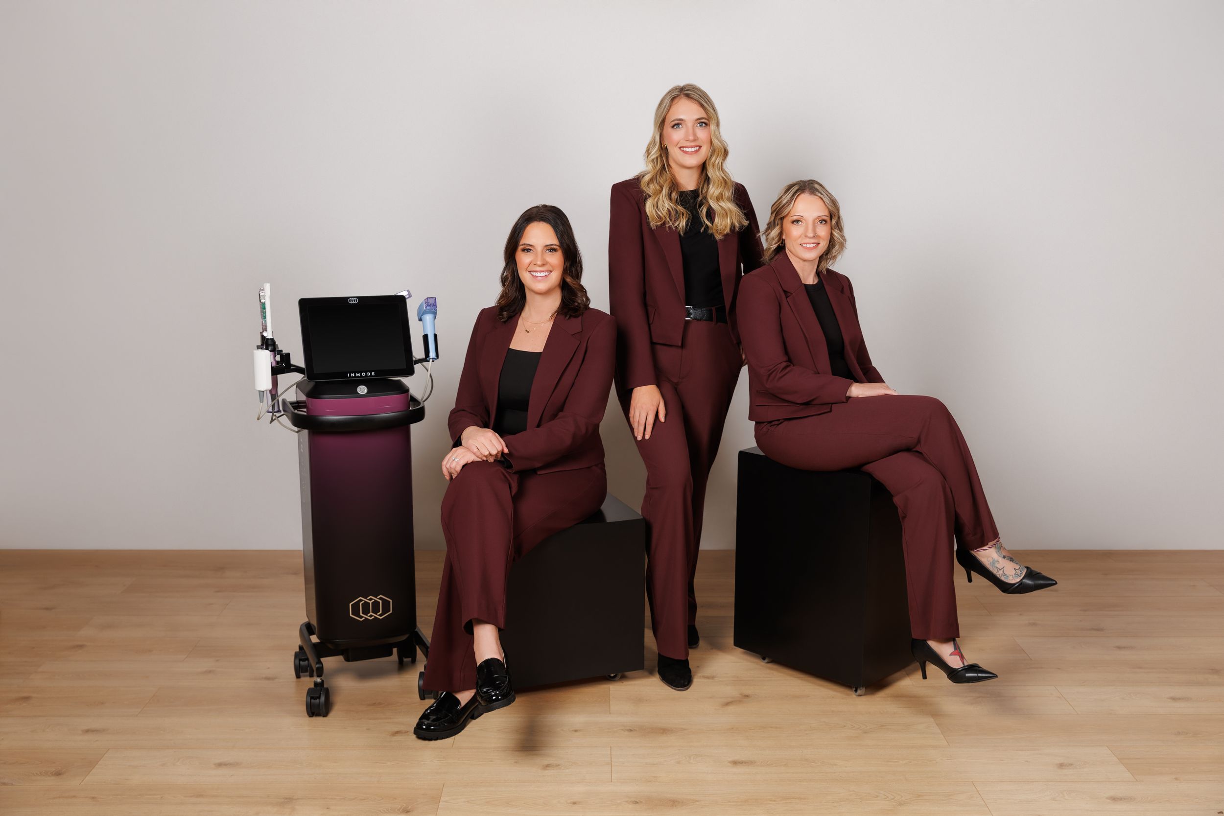 Professional studio portraits of people in burgundy business attire seated against a light gray backdrop.